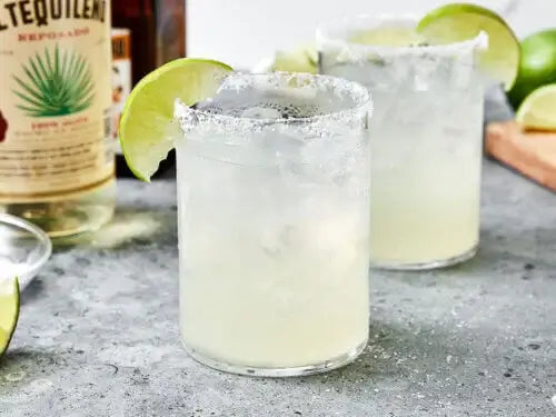 Classic margaritas with lime garnish on a countertop, accompanied by a bottle of tequila, perfect for cocktail enthusiasts.